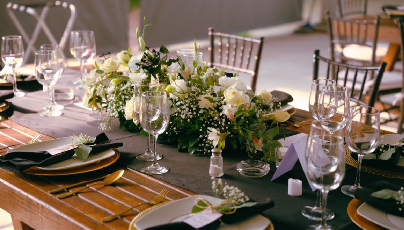 Centro de mesa de rosas blancas y gypsophila sobre mesa de madera con vajilla dorada